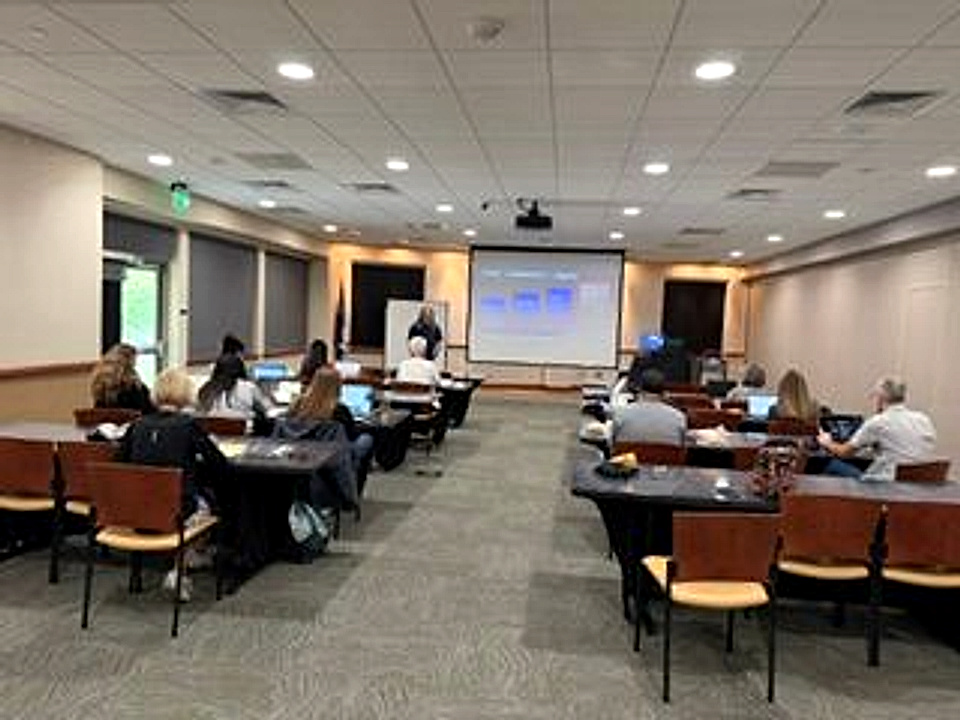 Colorado River Valley Chamber members seated at tables with laptops open, facing a projector screen, during a Hands On AI Lab workshop at Grand River Health in Rifle